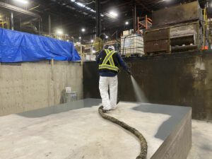 worker spraying waterproof resinous coating over primary containment system in a warehouse industrial facility