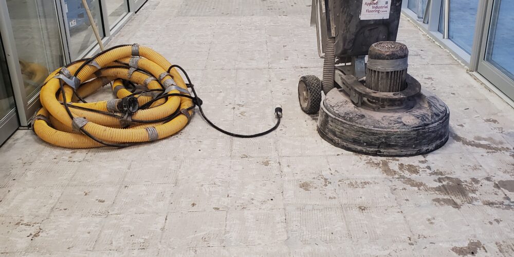 Préparation de la surface à l'aide d'un équipement de ponçage du béton à l'entrée d'un magasin Home Hardware en Ontario avant l'installation d'un revêtement de sol industriel MMA pour trafic intense.