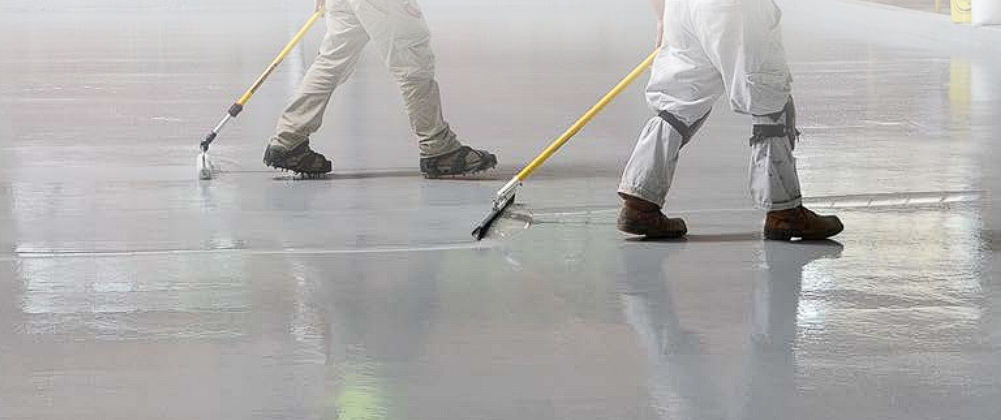 Two men installing epoxy flooring with rollers